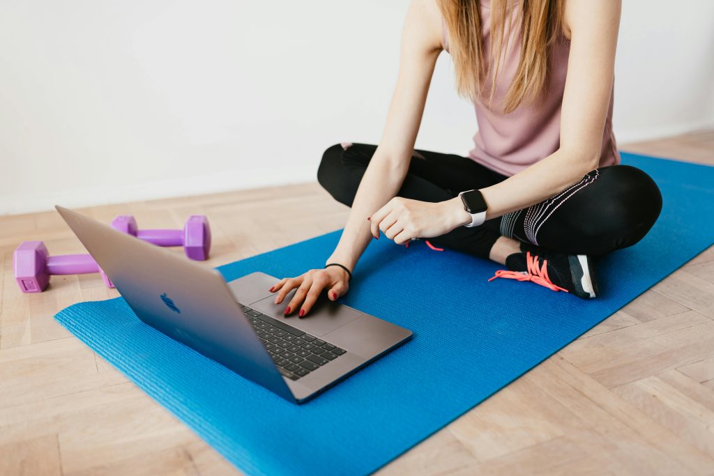 pexels-photo-4498475-4498475 Woman in activewear using a laptop on a yoga mat with dumbbells, representing a healthy lifestyle.