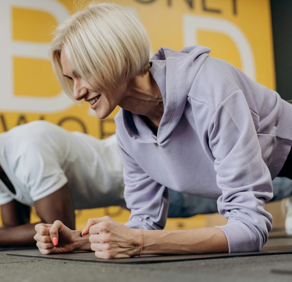 pexels-photo-6740309-6740309 Two adults in sportswear doing plank exercises in a gym, focusing on strength and fitness.