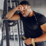 A man in a gym checks the time on his wristwatch while standing near exercise equipment