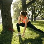 A woman stretches in the grass beside a tree, enjoying the outdoors and practicing her flexibility
