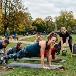 Group outdoor fitness class enjoying circuit training in a park amidst autumn trees, led by an enthusiastic instructor